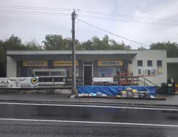 Budova prodejny od silnice se zbožím vyrovnaným před vchodem